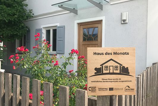 "Haus des Monats"-Plakette vor einem renovierten Eingangsbereich mit Rosen im Vorgarten